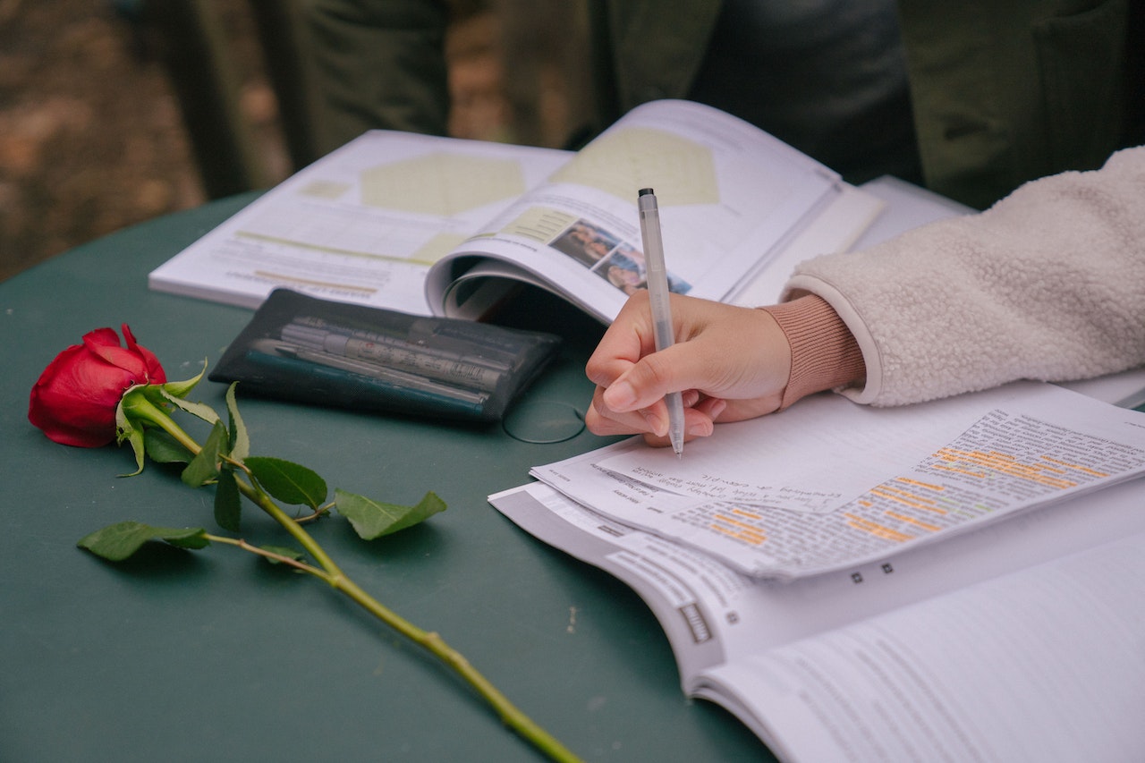 Faceless couple studying with textbooks while writing information on paper