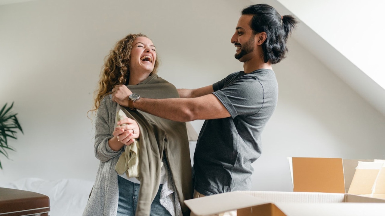 Happy couple unpacking boxes in new house and laughing