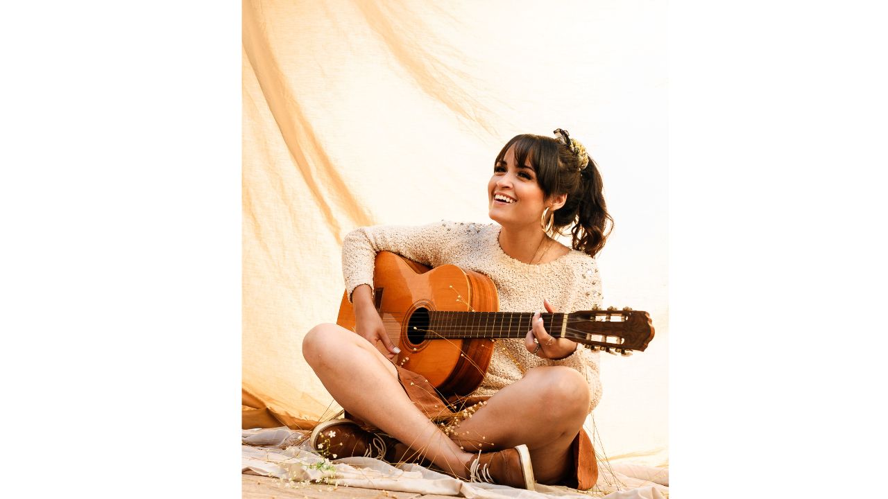 Delighted young ethnic female musician playing guitar on beach