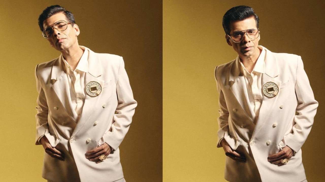 Karan Johar in suit with a telephone brooch & a dripping gold handbag